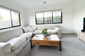 Uma sala de estar com um sofá bege, uma mesa de centro de madeira e uma televisão sobre um móvel.