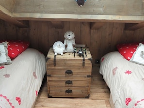 A cozy room with two beds, each with a red pillow and a white blanket with red patterns. In the center, there's a wooden chest with drawers and a small table with toys. - Charming apartment in the village - 8 guests (Arêches-Beaufort)