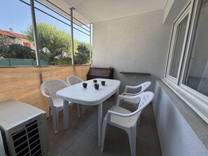 A balcony with a table and chairs, a grill, and a window. - Air-conditioned apartment - 4 guests (Argelès-sur-Mer)