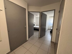 Een gang met twee deuren die leiden naar een slaapkamer met een bed en een raam.