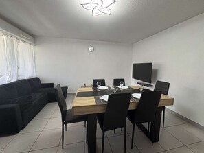 Un espace repas moderne avec une table en bois, des chaises noires et un téléviseur à écran plat.