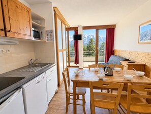 A kitchen with a sink, stove, and cabinets, leading to a dining area with a table and chairs. - Apartment with south-facing terrace - 6 guests (Chamrousse)