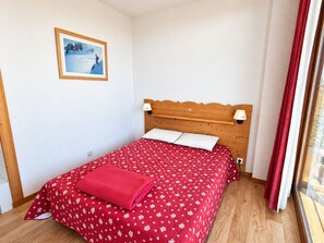 Habitació amb un llit, un panell de fusta al capçal, dues làmpades de nit, un quadre amb marc a la paret i una finestra amb cortines.