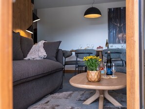 En moderne stue med en grå sofa, et rundt træbord med en vase med gule blomster, og et spiseområde med et træbord og stole.