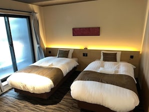 Hotellihuone, jossa on kaksi sänkyä, suuri ikkuna ja seinälle kiinnitetty taideteos.