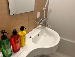 Pesualta kylpyhuoneessa, sen päällä kolme saippuapulloa ja peili.