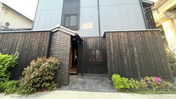 Un bâtiment moderne doté d’une grande entrée, d’une porte bien visible et d’un petit jardin agrémenté d’arbustes.