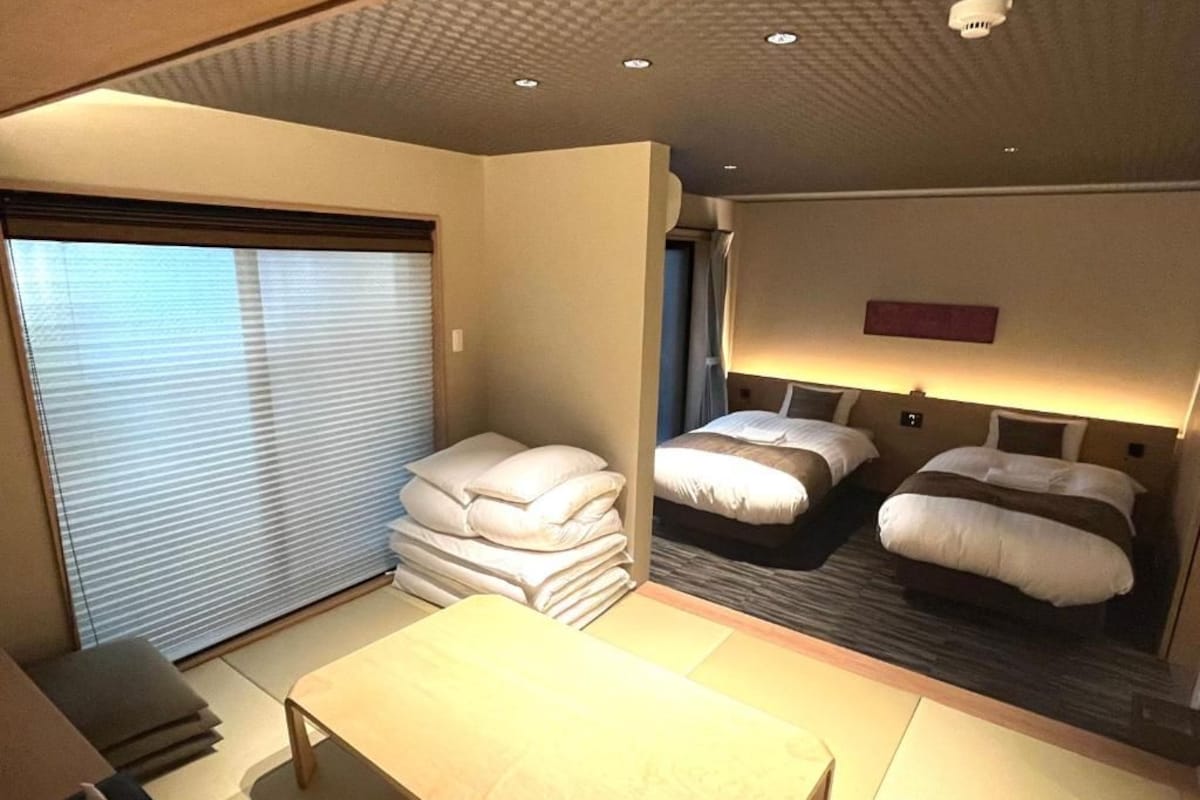 Hotellihuone, jossa on sänky, yöpöydät, työpöytä ja ikkuna, jossa on sälekaihtimet.