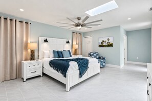 Ein modernes Schlafzimmer mit einem weißen Bett, zwei Nachttischen, einem Deckenventilator und einem Oberlicht.