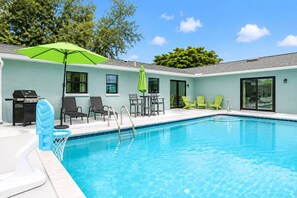 Ein Swimmingpool mit einer Terrassenanlage, inklusive Stühlen, einem Tisch und einem Grill.