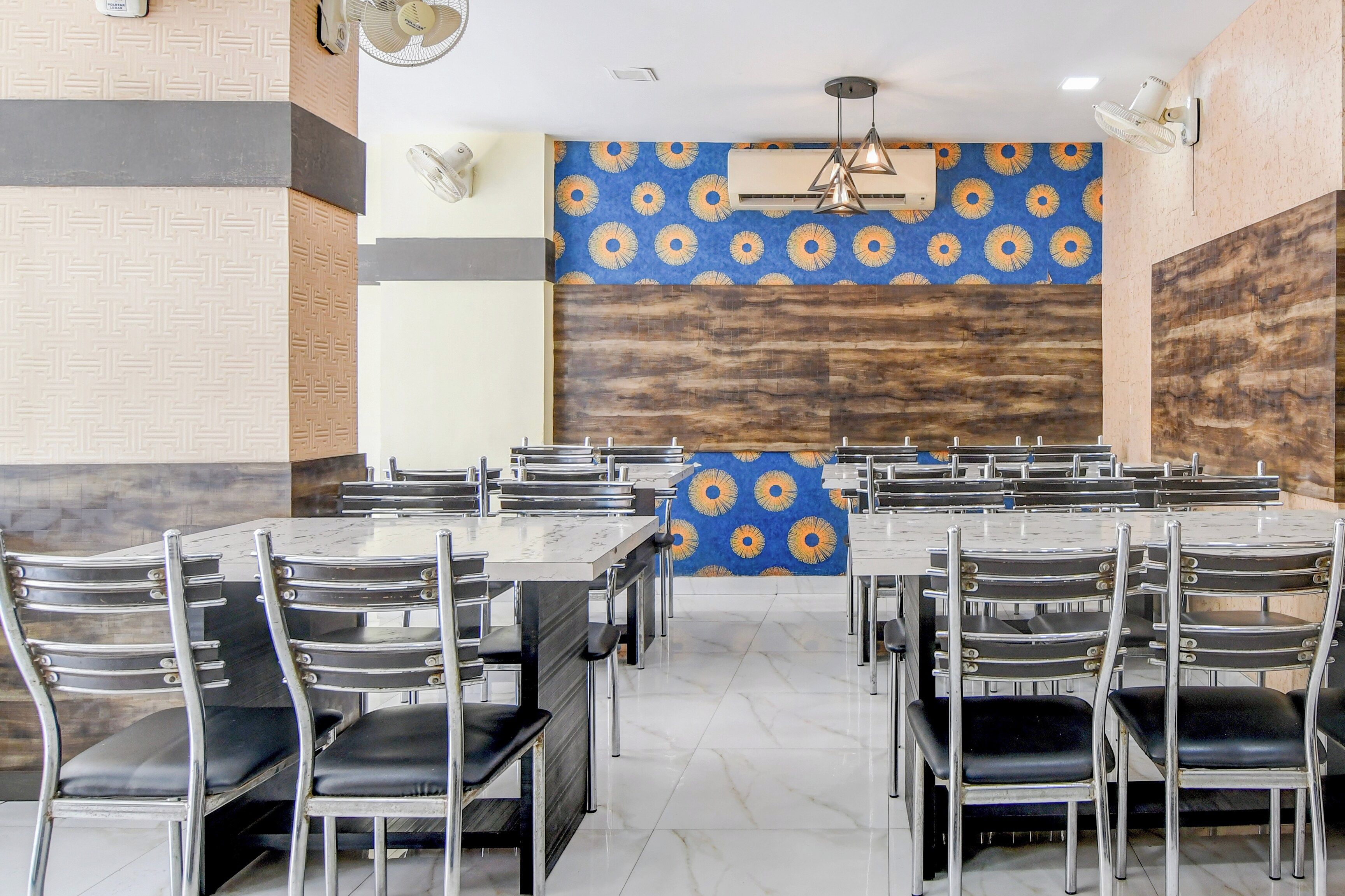 Comedor con varias mesas y sillas, un papel tapiz con diseño y un ventilador de techo.