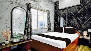 Habitación de hotel con cama, mesita de noche, espejo, ventana con cortinas y pared con diseño geométrico.