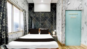 Habitación de hotel con cama, mesita de noche, lámpara, puerta y ventana con cortinas.