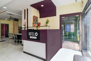 A hotel reception desk with a sign indicating it's company-serviced. There are chairs and a table in the background, and a door leading to another room. - Hotel O Serampore Railway Station (Shrirampur)