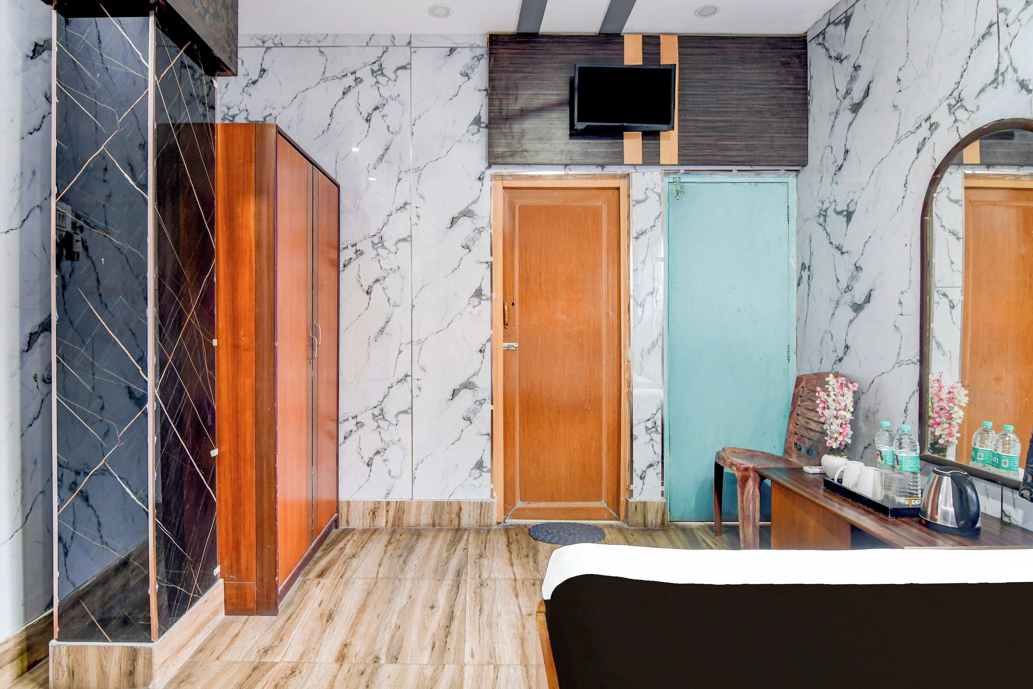 Habitación de hotel con cama, armario de madera, televisor montado en la pared, una mesita con un hervidor y un espejo.