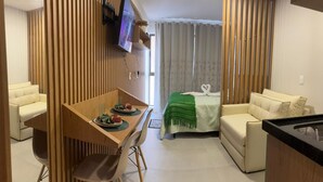 A hotel room with a dining area, a bed with a green blanket, and a TV mounted on the wall. - Vrbo Property (Porto de Galinhas)