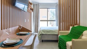 A hotel room with a bed, a dining table with plates and glasses, a green throw blanket, and a window with curtains. - Vrbo Property (Porto de Galinhas)