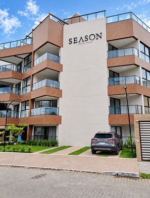 A multi-story building with a prominent 'SEASON SMART FLATS' sign, featuring balconies and a car parked in front. - Smart Flat Premium | Alexa | Porto City Center | 210 (Porto de Galinhas)