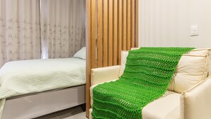A bedroom with a bed, a green knitted throw, a white chair, and a wooden panel wall. - Vrbo Property (Porto de Galinhas)