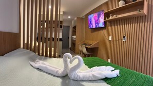 A hotel room with a bed, a TV mounted on the wall, a desk, and a green area rug. - Vrbo Property (Porto de Galinhas)
