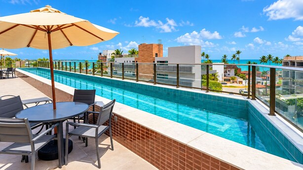 A rooftop pool with a glass balustrade, a table with chairs, and an umbrella. - Vrbo Property (Porto de Galinhas)