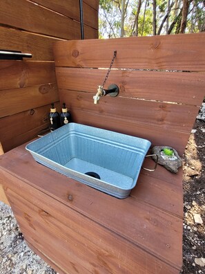 A wooden outdoor sink with a faucet, a blue basin, and two bottles of hand sanitizer.