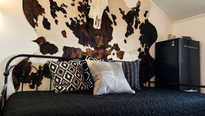 Et soveværelse med en væg beklædt med cowhide, en sort seng med mønstrede puder og en sort garderobe.
