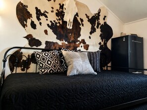 Ein Schlafzimmer mit Kuhfellwand, einem schwarzen Bett mit gemusterten Kissen und einem schwarzen Kleiderschrank.