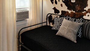 Et soveværelse med en seng, dekoration af et kranium fra en ko, en lampe og et vindue med gardiner.