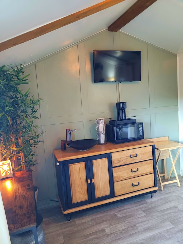 A kitchenette with a microwave, coffee maker, and a flat-screen TV mounted on the wall.