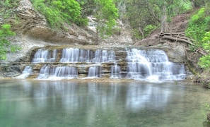 A waterfall cascading over a rocky ledge into a calm pool surrounded by greenery.