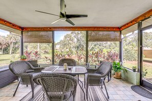 A covered patio area with a table and chairs, large windows, and a view of a garden. - 2BR Pet-Friendly – Walk or Bike to Manasota Beach (Englewood)
