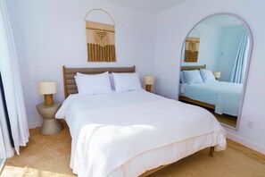 Une chambre à coucher comprenant un lit, deux tables de chevet, un miroir et une décoration murale en macramé.