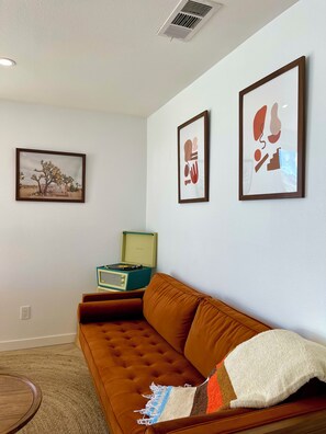 A living room with a brown sofa, a small table, and a framed picture on the wall.