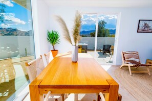 A spacious room with a wooden dining table, chairs, a potted plant, and a view of mountains through large windows.