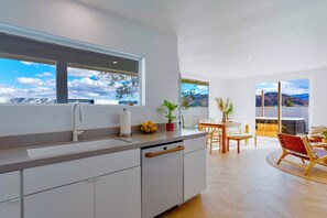 A modern kitchen with a large window, a dining area with a wooden table and chairs, and a view of mountains.