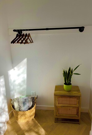 A room with a wooden floor, a woven basket, a small wooden side table with a plant, and a clothes drying rack.