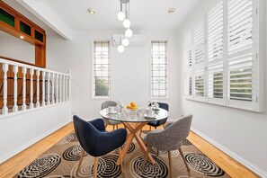 A dining area with a glass table, two chairs, a chandelier, and a view through a window with blinds. - Spacious Family Home with Multiple Living Areas (Baulkham Hills)