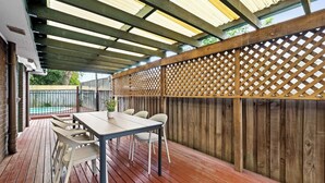 Eine Außenpatio mit Holzterrasse, einem Tisch mit Stühlen und einem Pool im Hintergrund.