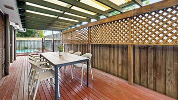 An outdoor patio with a wooden deck, a table with chairs, and a pool in the background.