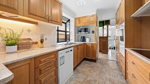 A modern kitchen with wooden cabinets, a dishwasher, a microwave, and a sink. - Spacious Family Home with Multiple Living Areas (Baulkham Hills)