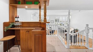 A wooden bar area with wine bottles and glasses, a stool, and a staircase with white balusters leading to an upper level. - Spacious Family Home with Multiple Living Areas (Baulkham Hills)