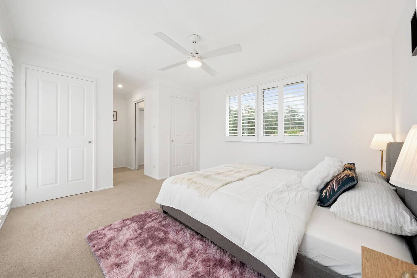 A bedroom with a bed, a ceiling fan, a window with blinds, and a door.