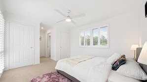 Ein Schlafzimmer mit einem Bett, einem Deckenventilator, einem Fenster mit Jalousien und einer Tür.