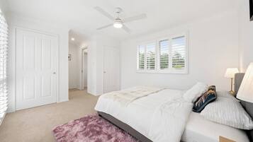 A bedroom with a bed, a ceiling fan, a window with blinds, and a door.