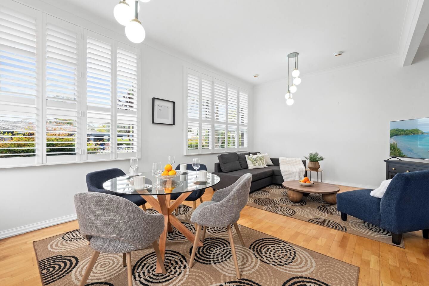 A modern living room with a glass dining table, sofas, and a TV.