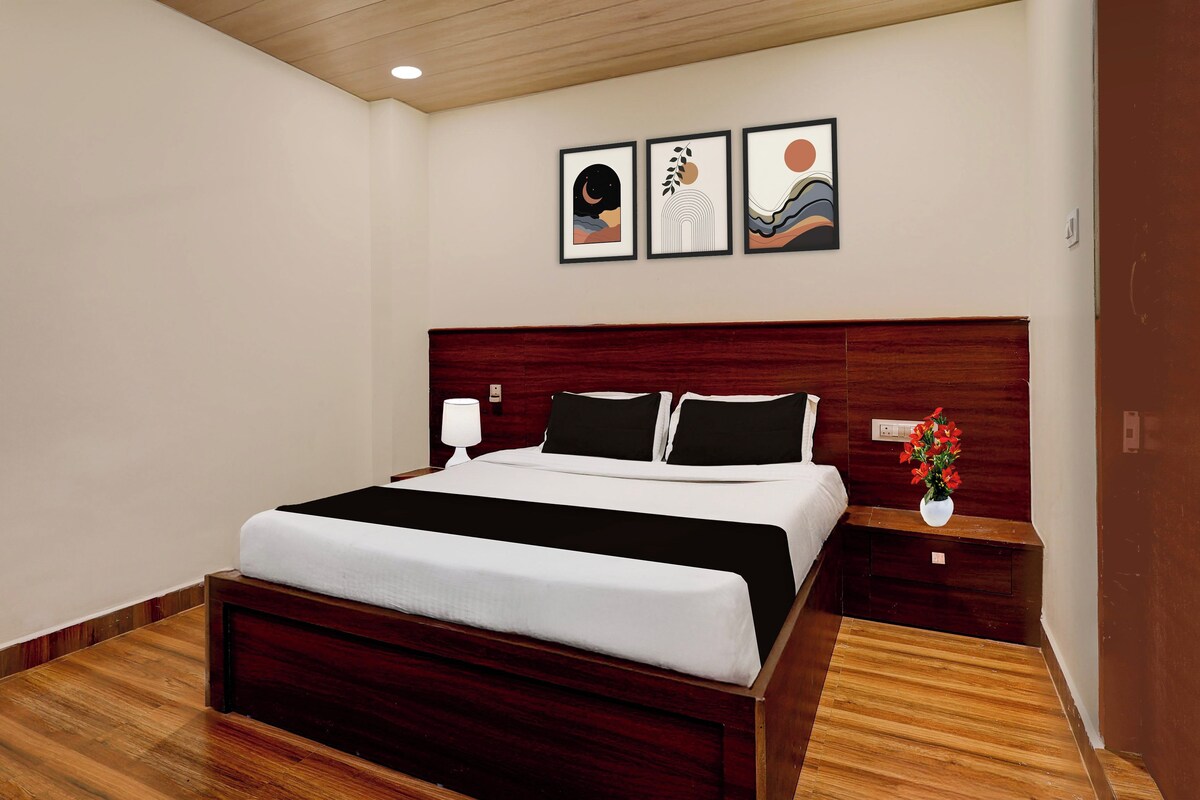 A hotel room with a large bed, a nightstand with a lamp, and three framed artworks on the wall.