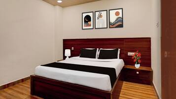 A hotel room with a large bed, a nightstand with a lamp, and three framed artworks on the wall.