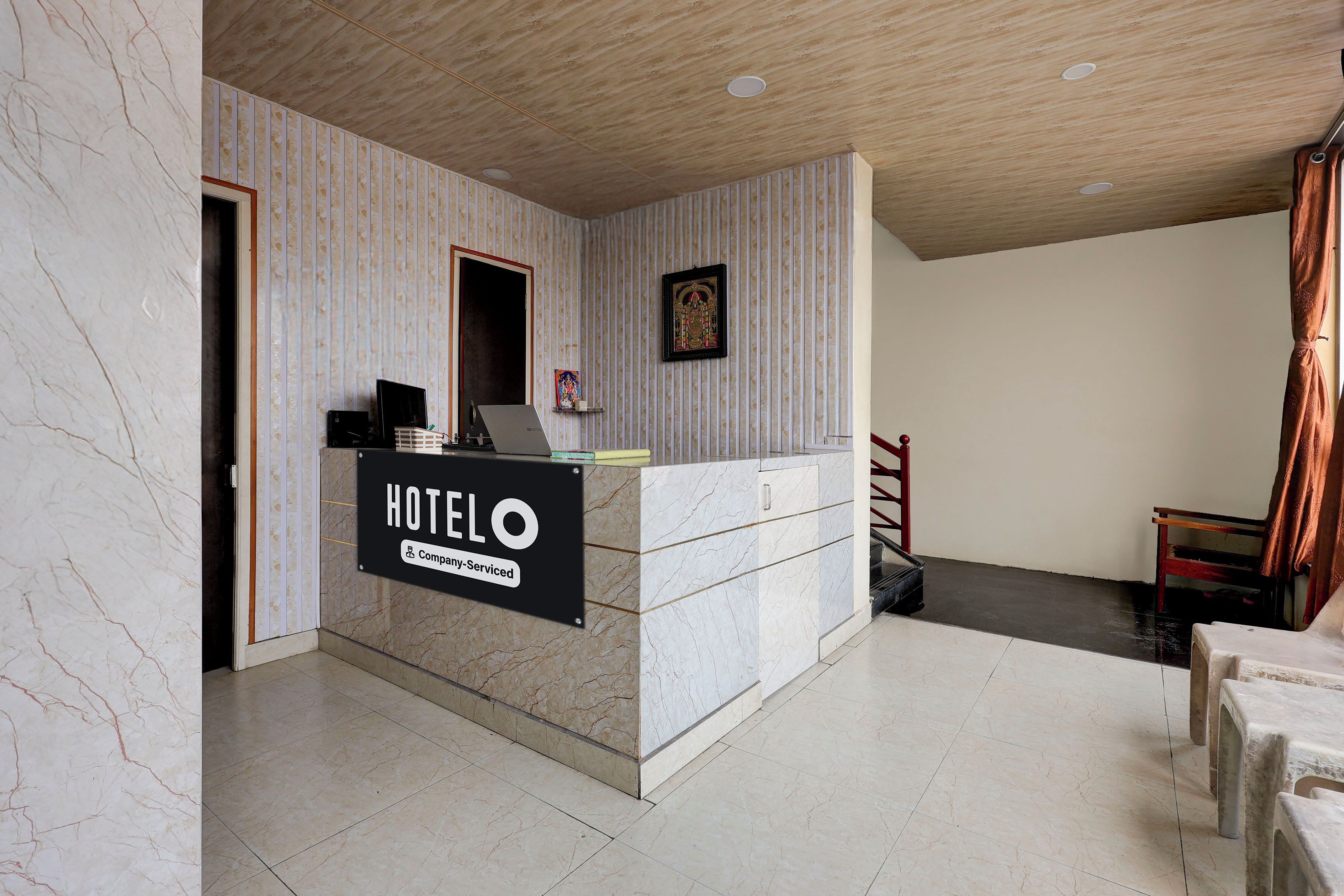A hotel reception desk with a sign indicating it's company-serviced, a framed picture on the wall, and a staircase leading to another area.