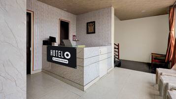 A hotel reception desk with a sign indicating it's company-serviced, a framed picture on the wall, and a staircase leading to another area.